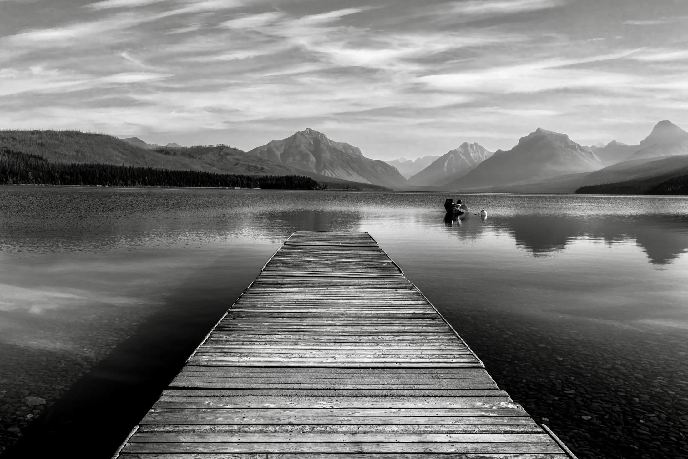 A wooden dock leading into a still lake framed by Glacier National Park mountains
